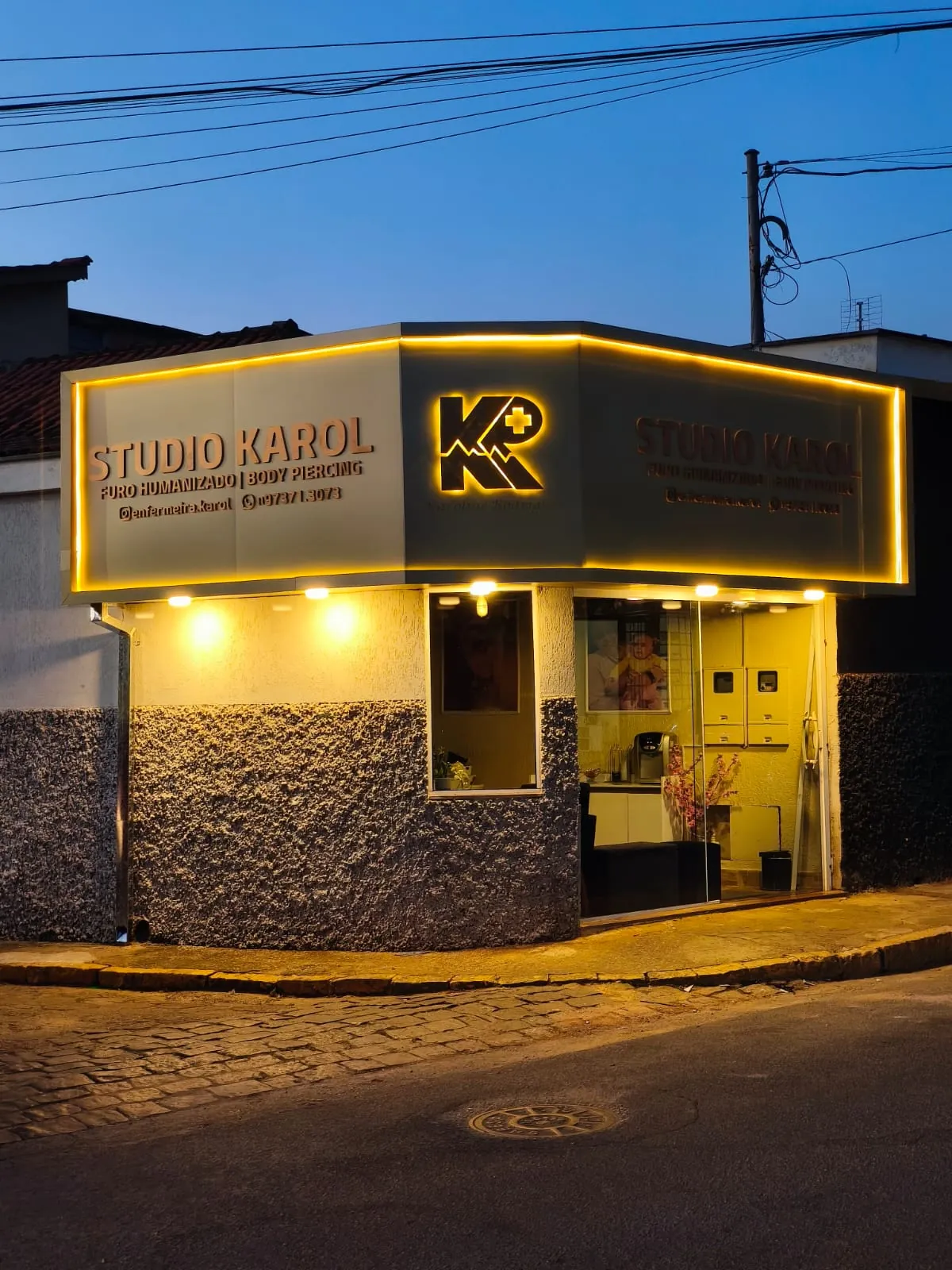 Fachada do Studio Karol com letreiro e logotipo iluminados ao anoitecer